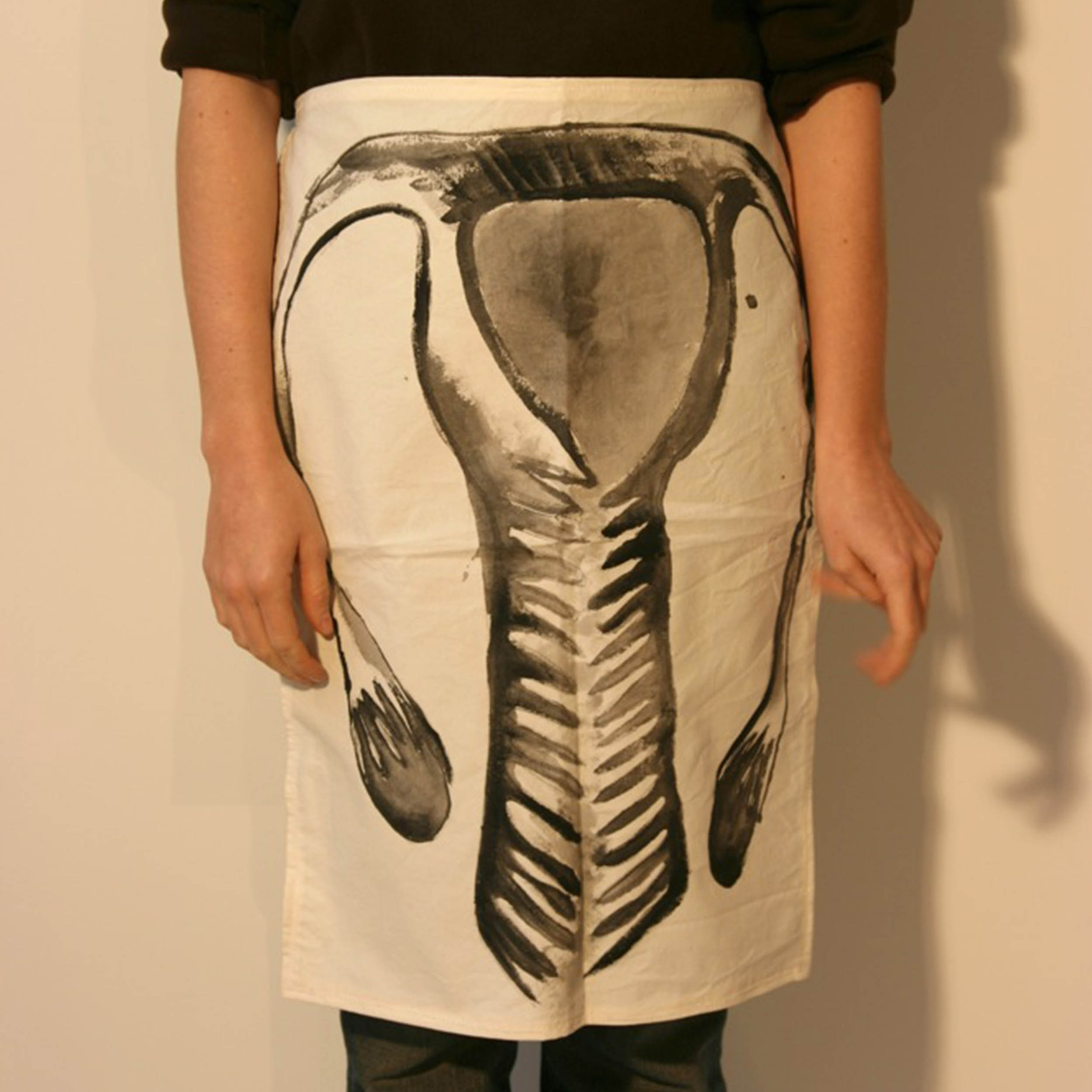 A person wears an apron from the waist down that depicts a stylized version of the female reproductive system.