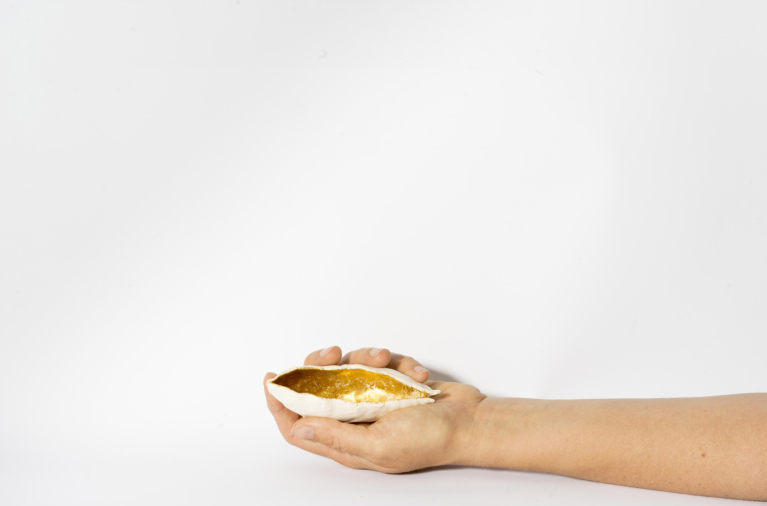 A hand holds a ceramic depiction of a seed pod that is painted gold inside.