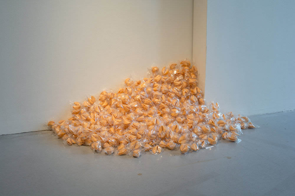 An artwork comprised of several wrapped fortune cookies arranged to look like they've been spilled in a corner.