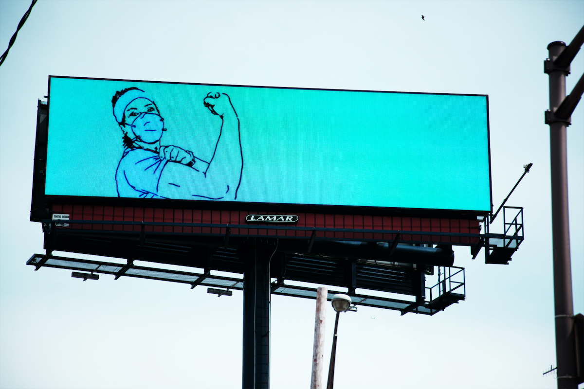 A photograph of a billboard depicting an animation of a healthcare worker with their bicep curled like Rosie the Riveter.